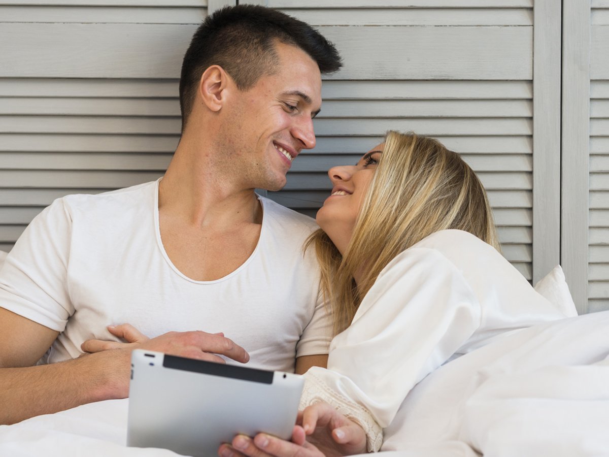 Coito Programado, Casal Deitado na Cama Sorrindo.