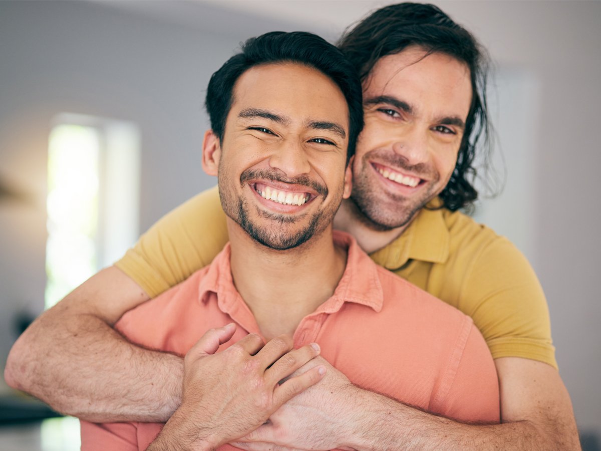 Casal LGBTQIA+ se abraçando e sorrindo.